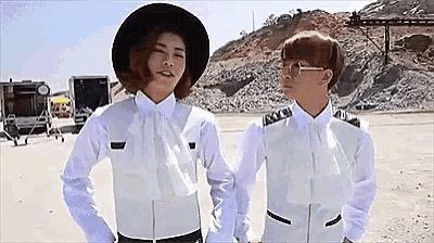 two women in white shirts and hats are standing next to each other in a field holding hands .