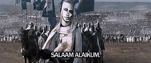 a man with a mask on his face is standing in front of a crowd of soldiers and says salaam alaikum .