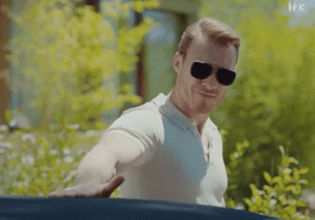 a man wearing sunglasses and a white shirt is reaching out his hand towards a car window .