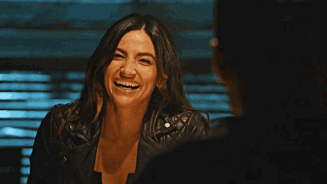 a woman in a leather jacket is smiling and laughing