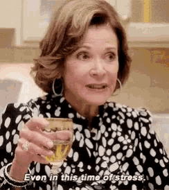 a woman is holding a glass of wine in her hand and saying `` even in this time of stress . ''