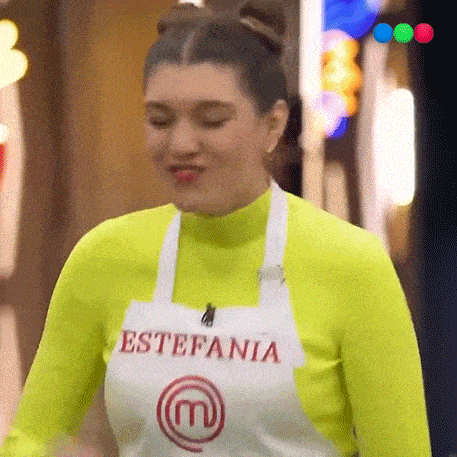 a woman wearing a yellow sweater and an apron with the letter m on it is making a funny face .
