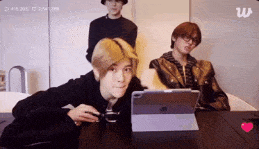 a group of young men are sitting at a table using a tablet computer .