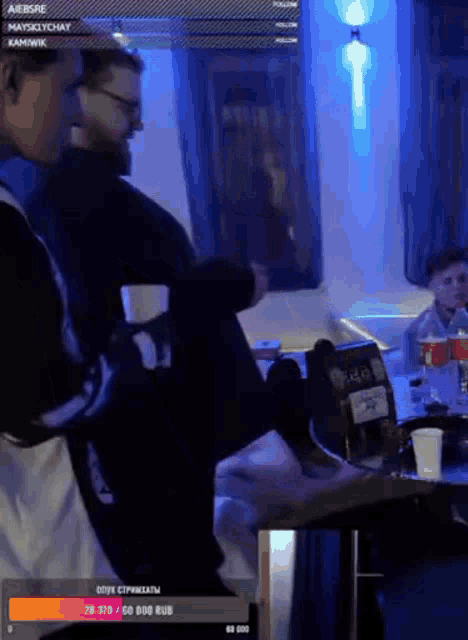 a group of people are sitting around a table in a dark room with a blue light behind them .