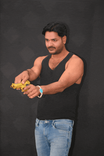 a man in a black tank top and blue jeans holds a toy gun