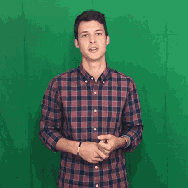a young man in a plaid shirt is standing in front of a green screen .