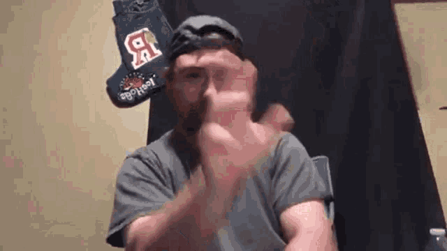 a man wearing a baseball cap and a t-shirt with the letter r on it is making a funny face .