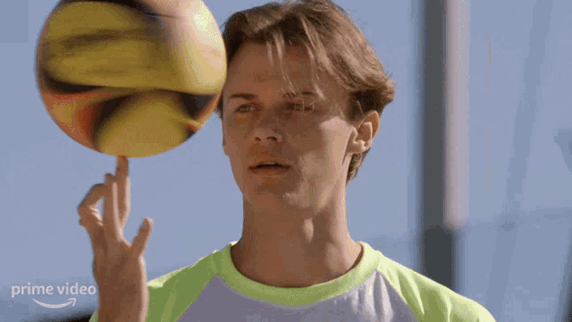a man in a green shirt is balancing a yellow ball on his finger with a prime video logo in the corner