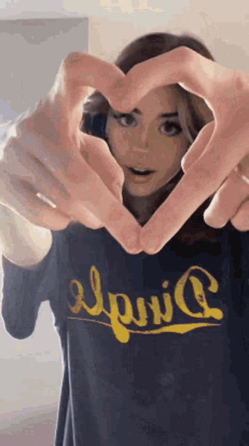 a woman in a blue shirt is making a heart shape with her fingers .