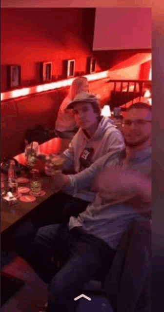 a group of people are sitting at a table in a bar holding drinks .