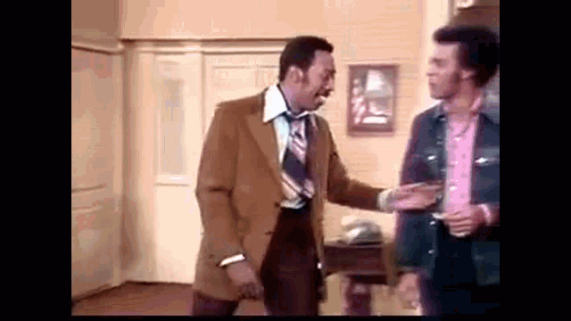 two men are standing next to each other in a room and talking .