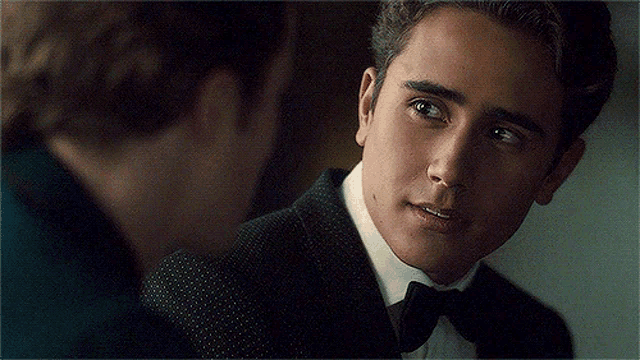 a man in a suit and bow tie is looking at another man in a suit .