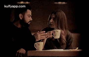 a man and a woman are sitting at a table drinking coffee from cups .