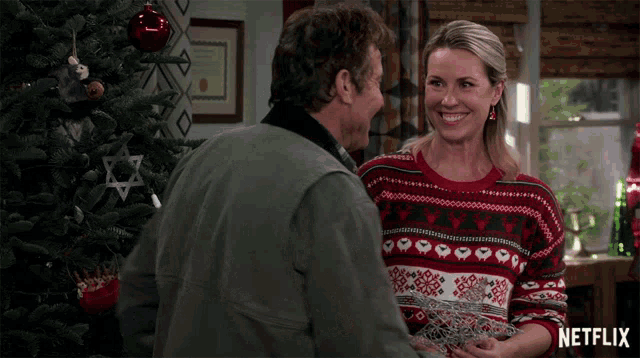 a man and a woman standing in front of a christmas tree with a netflix logo on the bottom