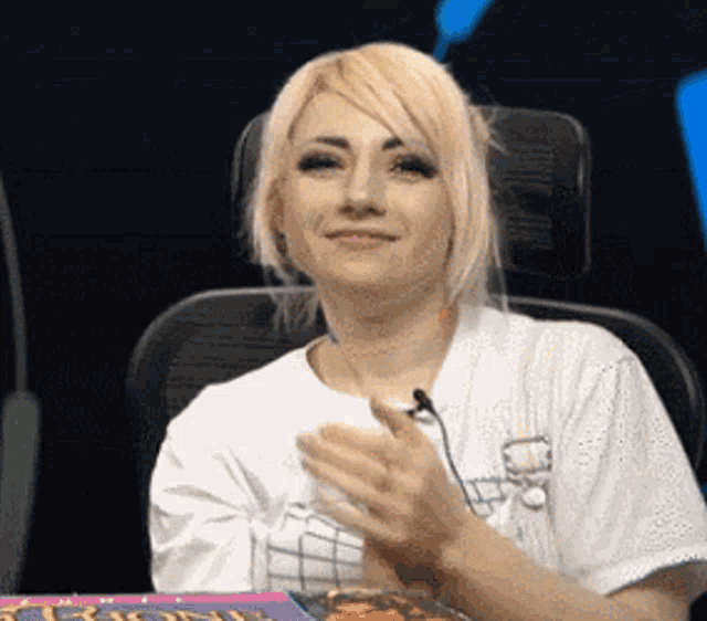 a woman in a white shirt is sitting in front of a microphone and applauding