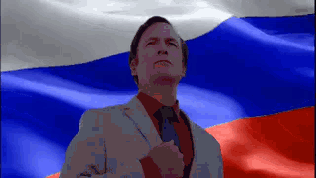 a man in a suit and tie stands in front of a waving russian flag