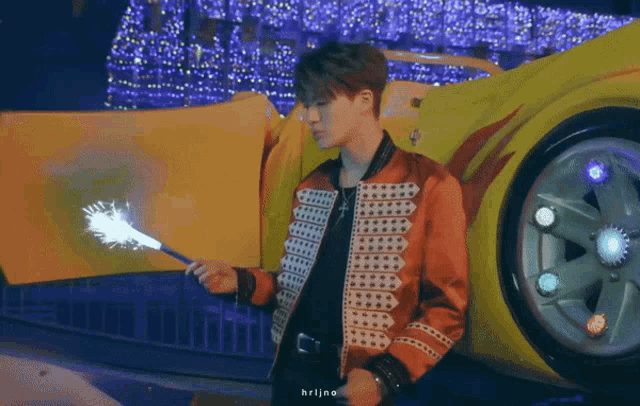 a man is holding a sparkler in front of a yellow car with flames on it