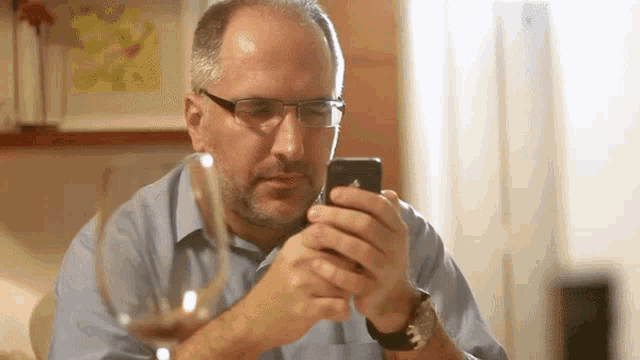 a man wearing glasses and a watch looks at his phone