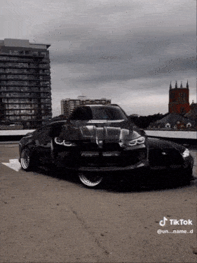 a black car is parked in a parking lot with buildings in the background