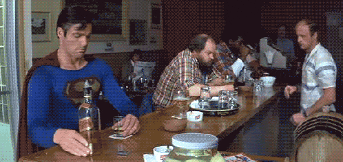 a man in a superman costume sits at a bar holding a bottle