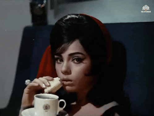 a woman is eating a piece of bread and drinking from a cup that says ni studios on it