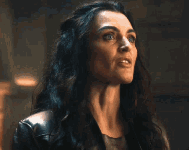 a woman with long dark hair and blue eyes is wearing a leather jacket .