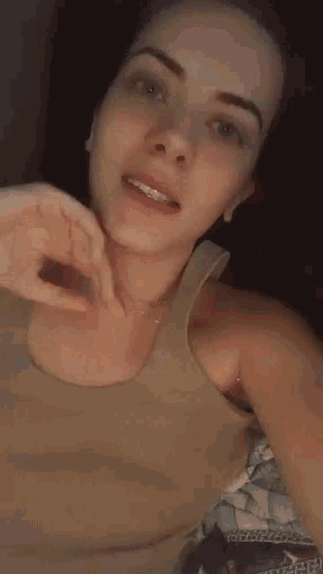 a woman in a tank top is making a funny face while laying on a bed .