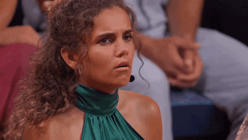 a woman with curly hair wearing a green dress looks surprised