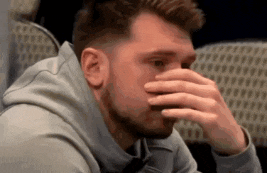 a man with a beard is covering his face with his hand while sitting in a chair .
