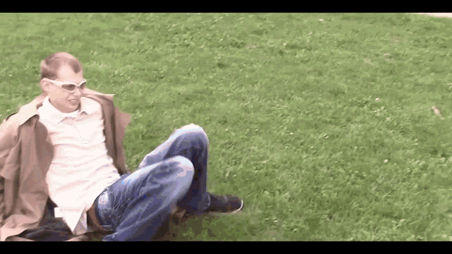 a man wearing sunglasses and a trench coat is laying on the grass