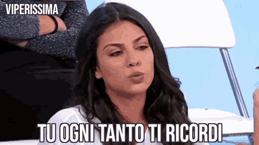 a woman is sitting in a chair with her arms crossed and says " tu ogni tanto ti ricordi " .
