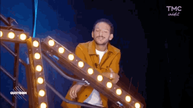 a man in a yellow jacket is standing in front of a bunch of lights on a stage ..