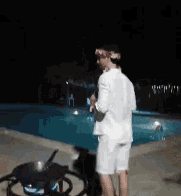 a man in a white shirt and shorts is standing in front of a swimming pool at night