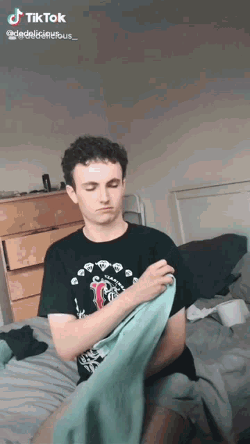 a young man is sitting on a bed holding a towel and a tiktok video is displayed below him