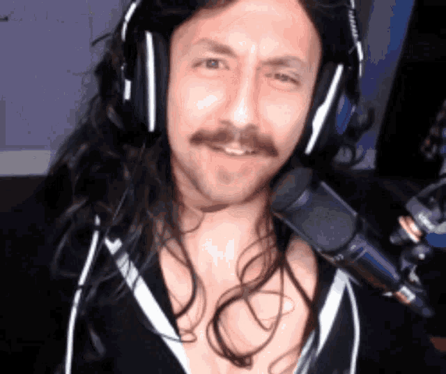 a man with long hair and a mustache wearing headphones stands in front of a microphone