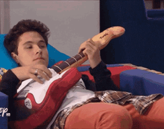 a young man laying on a bed playing a guitar