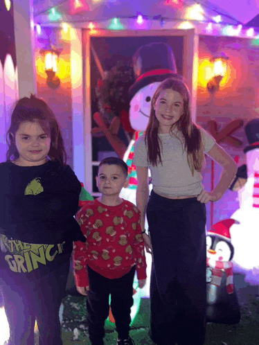 a girl wearing a grinch sweater stands with two other children