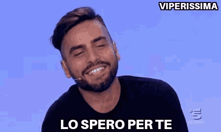a man with a beard is smiling and saying `` lo spero per te '' while wearing a black shirt .