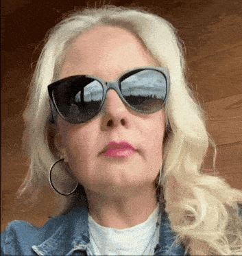 a woman wearing sunglasses and hoop earrings is looking at the camera