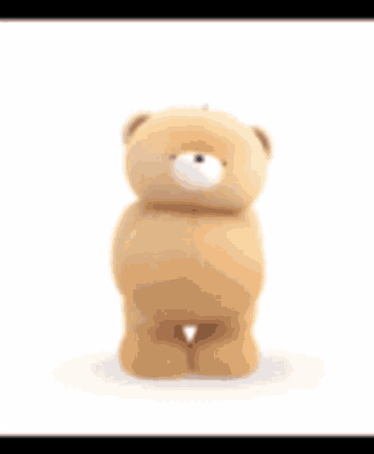 a brown teddy bear is standing on a white surface and waving his arm .