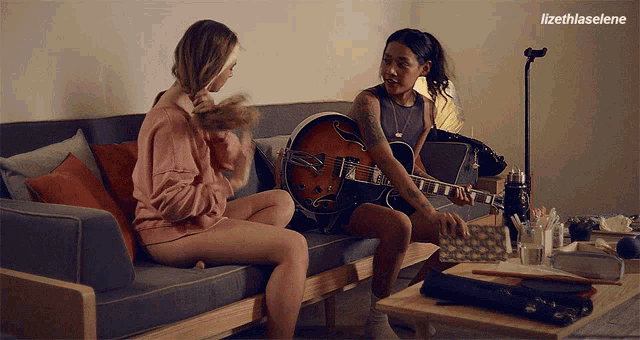 two women sitting on a couch with one holding a guitar and the caption lizethlaselena
