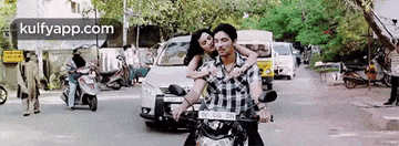 a man and woman are riding a motorcycle down a busy street .