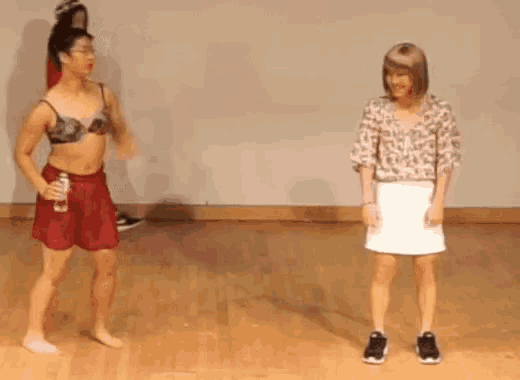a man in a bra and shorts is dancing with a woman in a skirt .