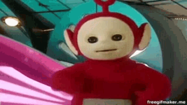 a red teletubbies stuffed animal is standing in a room with a pink background .