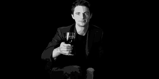 a man in a suit is holding a glass of wine in his hand .