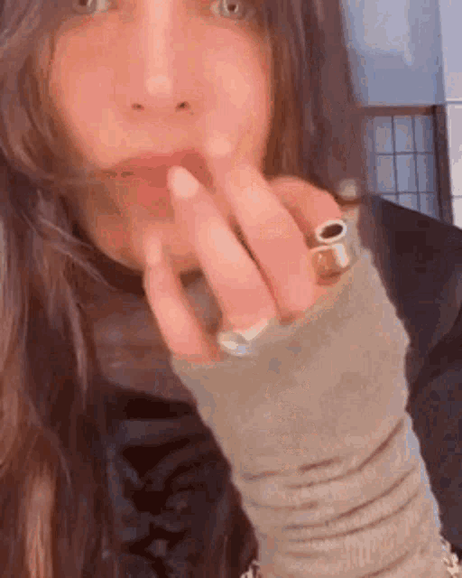 a woman with a ring on her finger is holding her finger to her mouth .