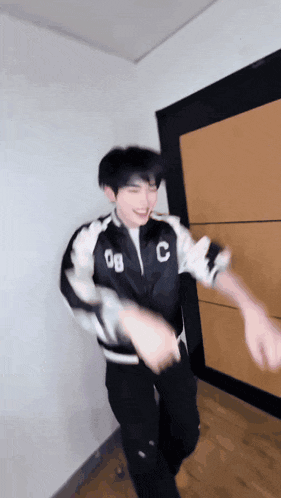 a young man wearing a jacket with the letter c on it is dancing in a room .