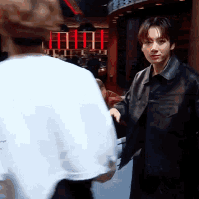 a man in a leather jacket is standing next to another man in a white shirt in a restaurant .