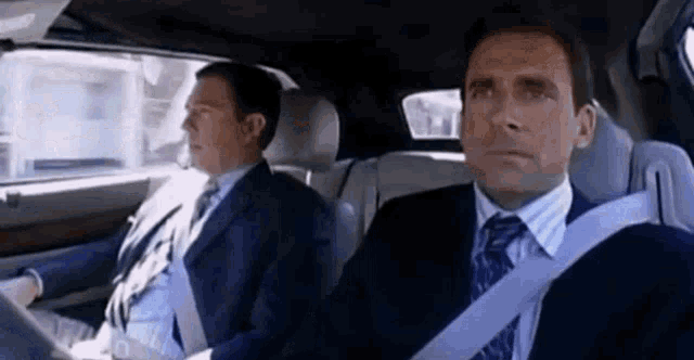 two men in suits and ties are sitting in a car with seat belts on .