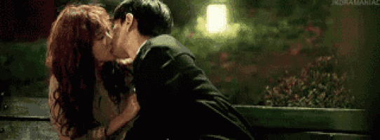 a man and woman are kissing on a bench at night .